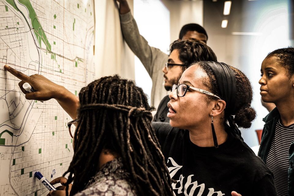 Mo in middle of four mixed gender undergrad students pointing to a city map of Philadelphia for mapping disparity workshop.